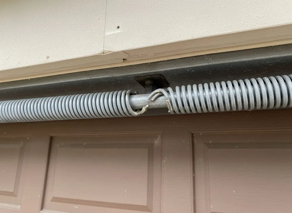 A broken torsion spring with a visible gap in the coil above a garage door