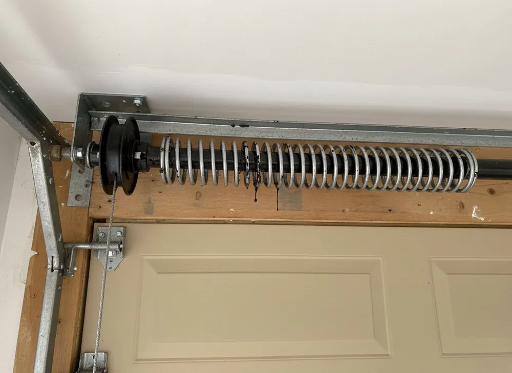 Close view of a torsion spring and cable drum above a garage door
